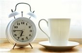 Photo of an alarm clock next to a coffee cup