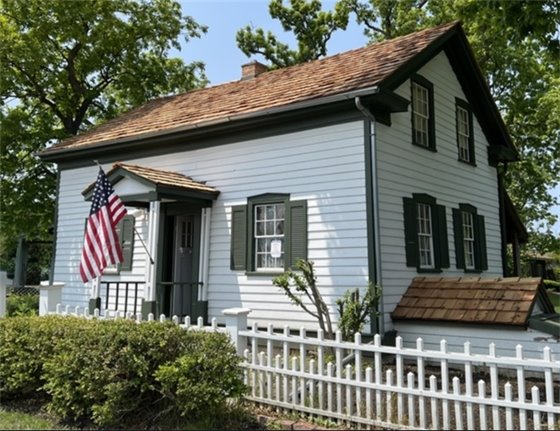 Photo of the Luther House with white paint and green trim with an American flag attached next to the front door