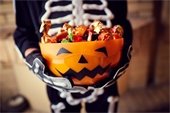 Photo of a child dressed at a skeleton for Halloween and holding a big bowl of candy