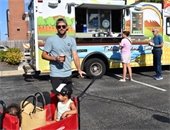 Photo of a child in a wagon being pulled by a man in front of a food truck