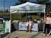 A picture of the Sustainability Commission's tent at the Farmers Market with two children playing a recycling game