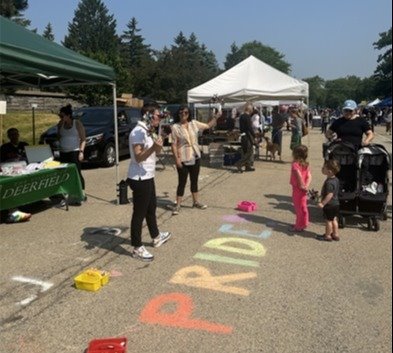 Photo of people at the Farmers Market and it says PRIDE in colorful chalk on the street
