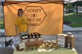 Photo of honey vendor booth at the farmers market with a yellow backdrop that reads Honey House with a variety of honey-related products on display for sale
