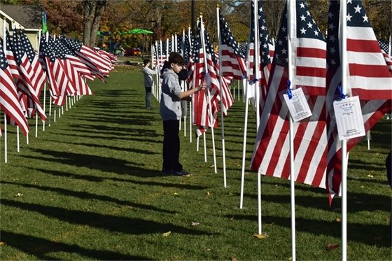 Photo of two teenage boys tying dedication cards to a row of American flags at Jewett Park 