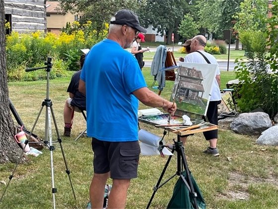 Photo of a man at an easel painting the Ott Cabin at the Historic Village 