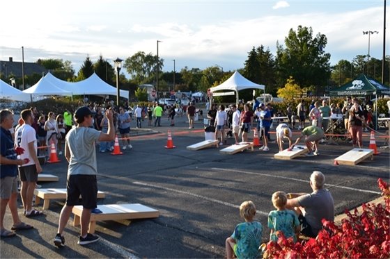 Children sit on a curb watching people play bags at Harvest Fest