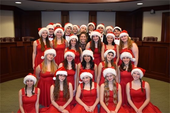 A photo of the DHS Choraliers warming up in Village Hall before a performance in red dresses for girls and tuxedoes and red bowties for the boys