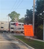 Orange construction sign reading "Railroad Repairs Begin August 4" in front of a Metra Train crossing Osterman Ave